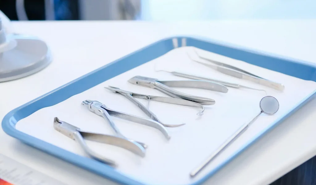 A stainless steel dental and orthodontic instrument tray organized on a paper liner,